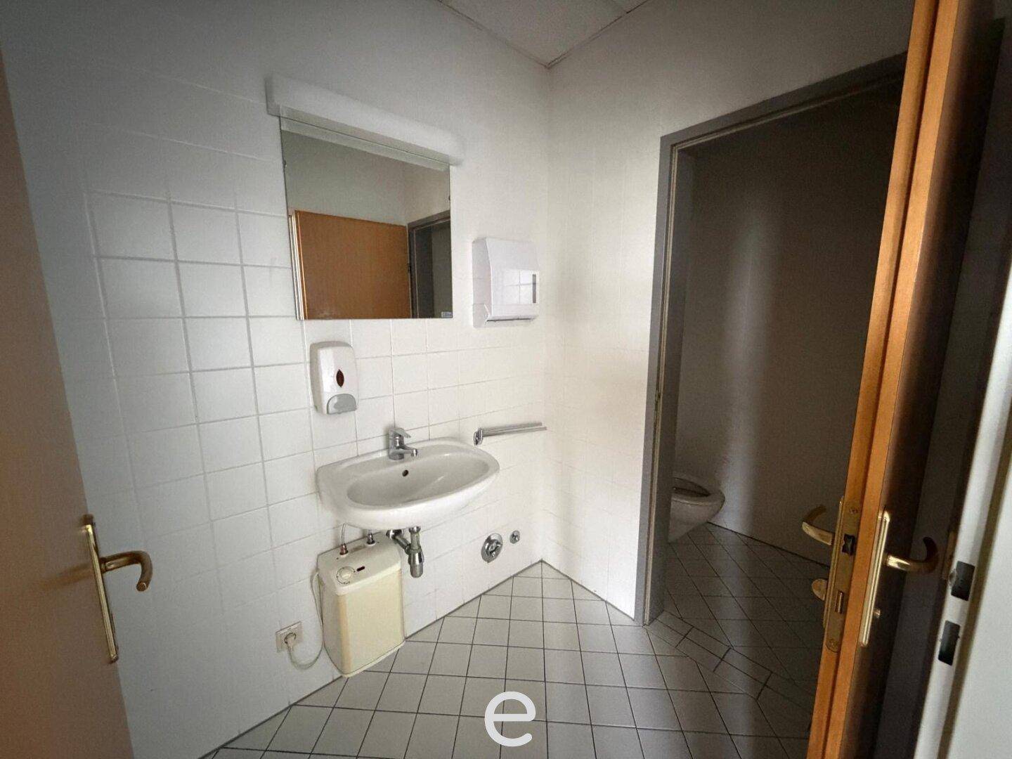 Einfache Toilette mit Waschbecken, Spiegel und weißen Fliesen, funktional und sauber.