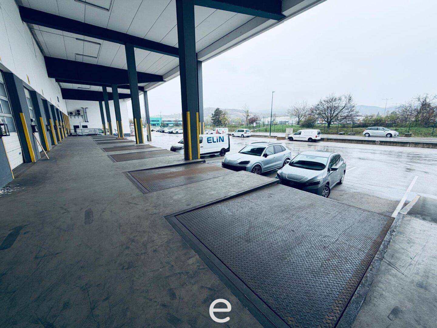 Außenbereich mit mehreren Laderampen und geparkten Fahrzeugen, ideal für Logistik und Warenverkehr.