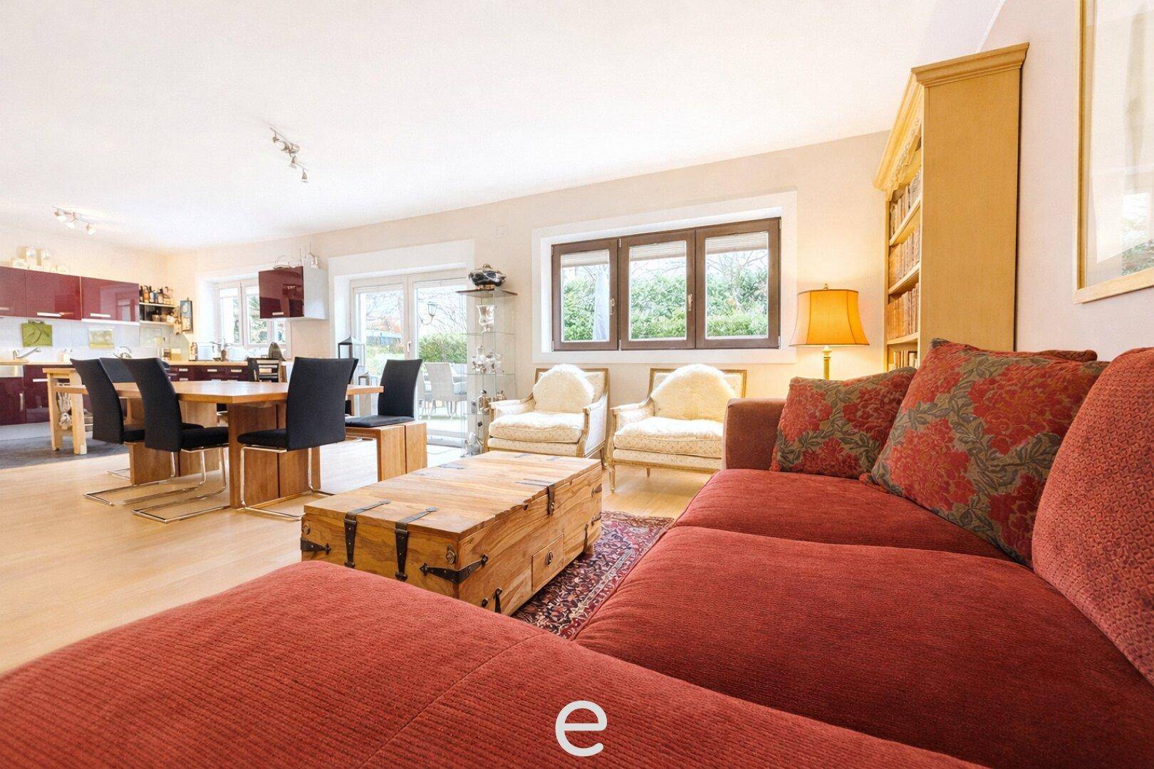 Heller, offener Wohn-Essbereich mit rotem Sofa, Holztisch und integrierter Küche im Hintergrund.