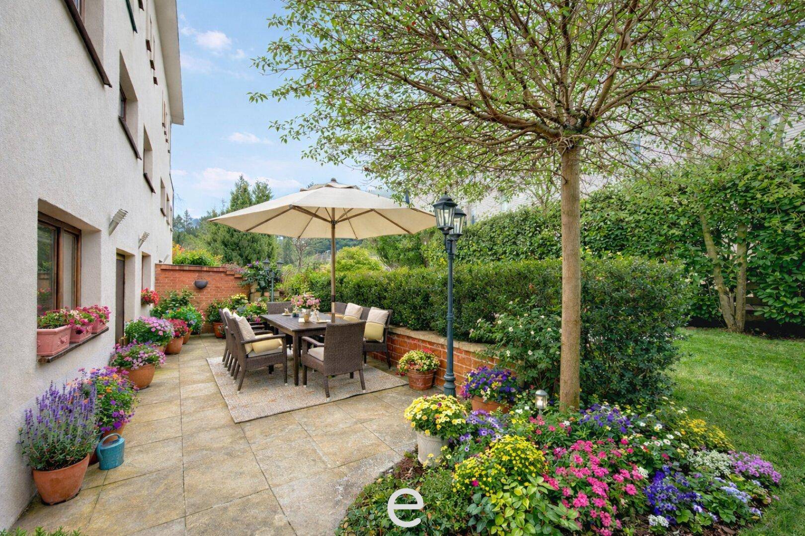 Gemütliche Terrasse mit Sonnenschirm, Gartenmöbeln und farbenfrohen Blumenbeeten in einem gepflegten Garten.