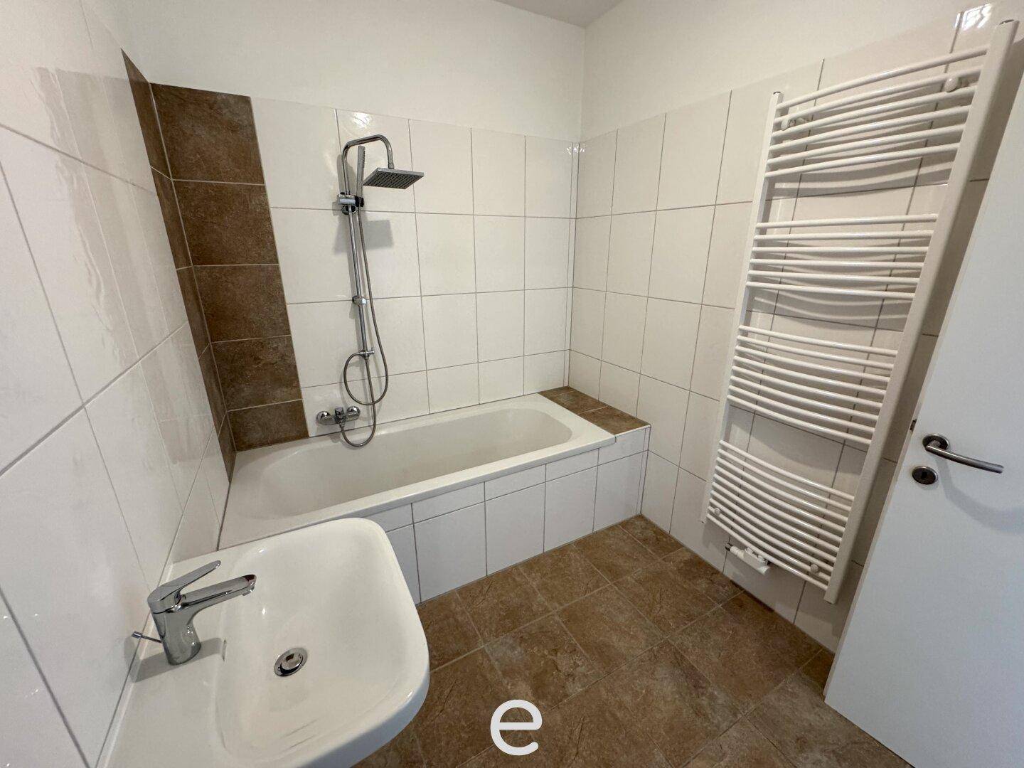 Gefliestes Badezimmer mit Badewanne, Dusche und beheiztem Handtuchhalter.