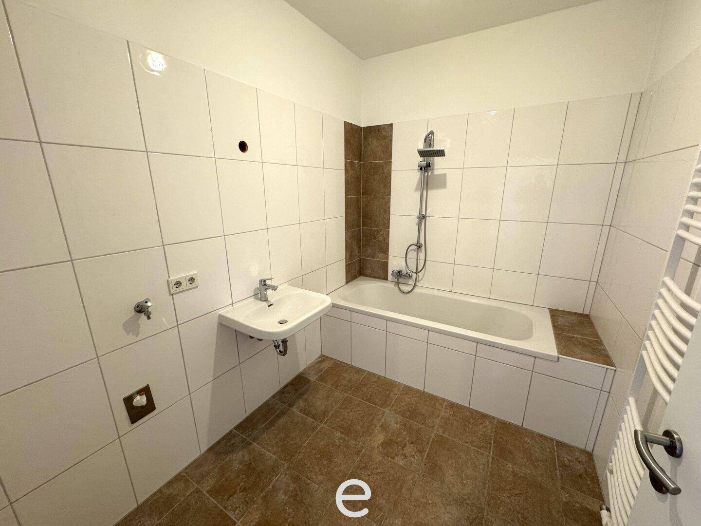 Funktionales Badezimmer mit Badewanne, Duscharmatur und Fliesen in Braun-Weiß.
