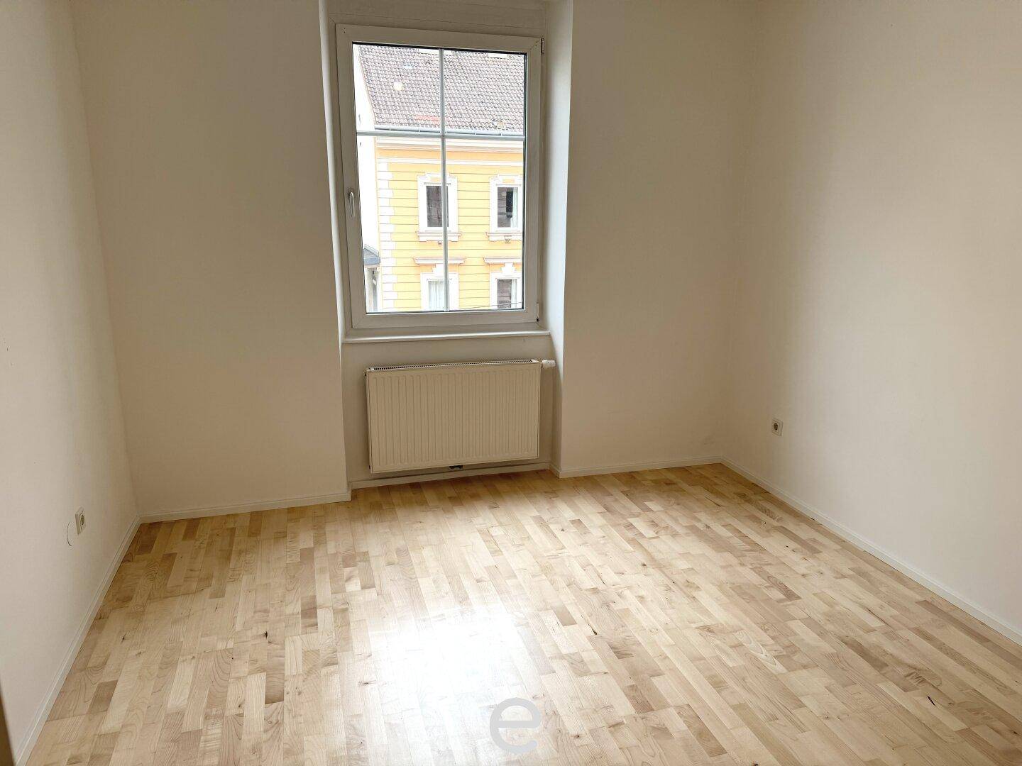 Helles Schlafzimmer mit Parkettboden und Blick auf die gegenüberliegende Bebauung.