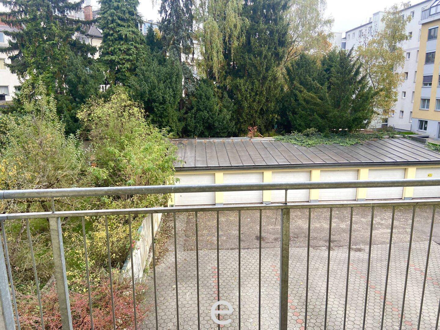 Blick vom Balkon auf Garagen und grüne Bäume im Hinterhofbereich.