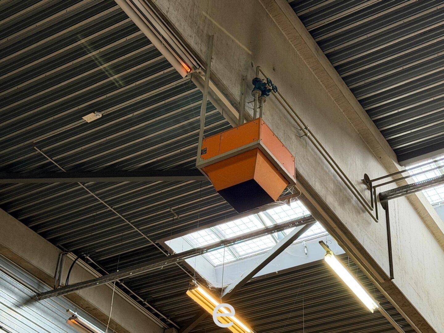 Detailaufnahme der Deckenkonstruktion mit Beleuchtung und Lüftungselementen in einer Industriehalle.