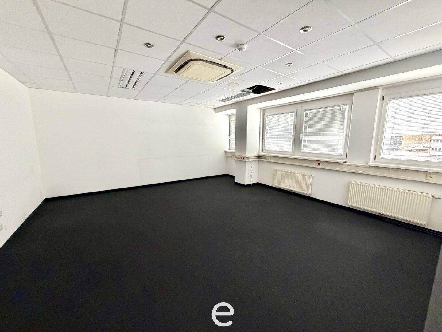 Modernes Büro mit dunklem Teppichboden, Klimaanlage und großen Fenstern, ideal für konzentriertes Arbeiten.
