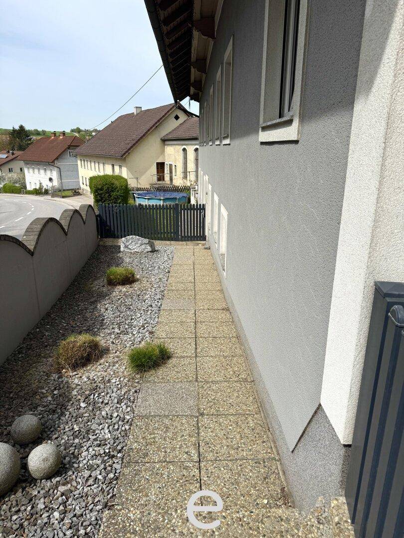Schmaler Weg entlang der Hausfassade mit Kiesbeet und kleinen Pflanzen.