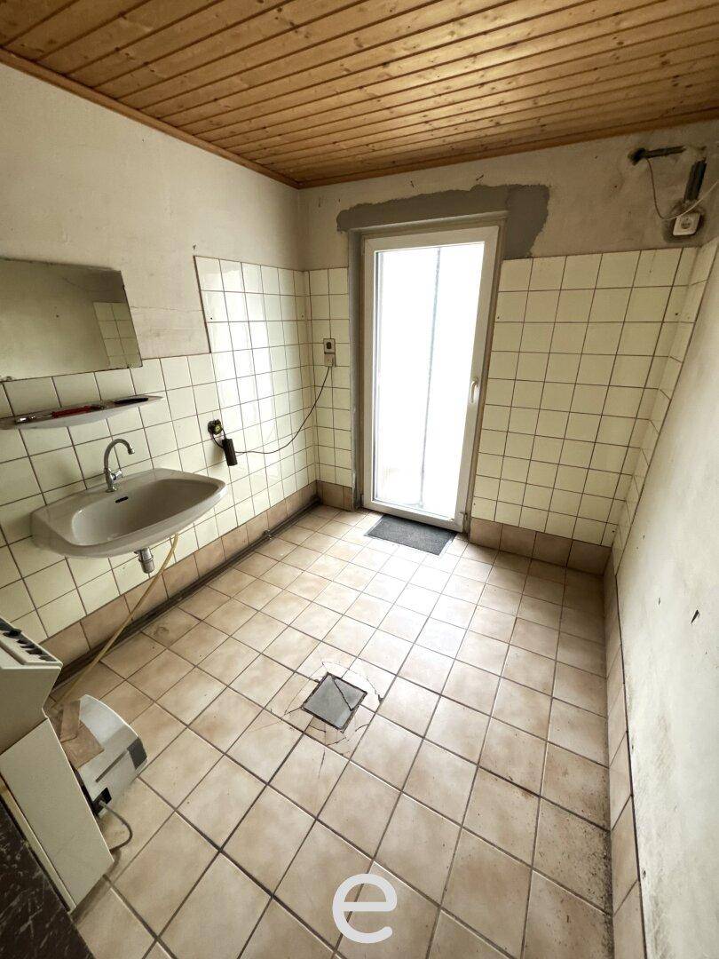 Kellerraum mit Fliesenboden, Waschbecken und Zugang nach draußen.