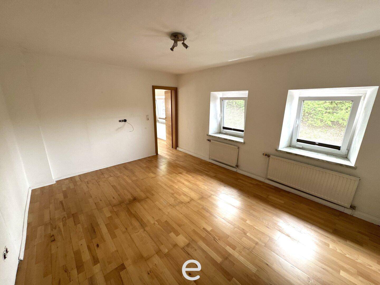 Helles Schlafzimmer mit Holzboden, weißen Wänden und zwei Fenstern.
