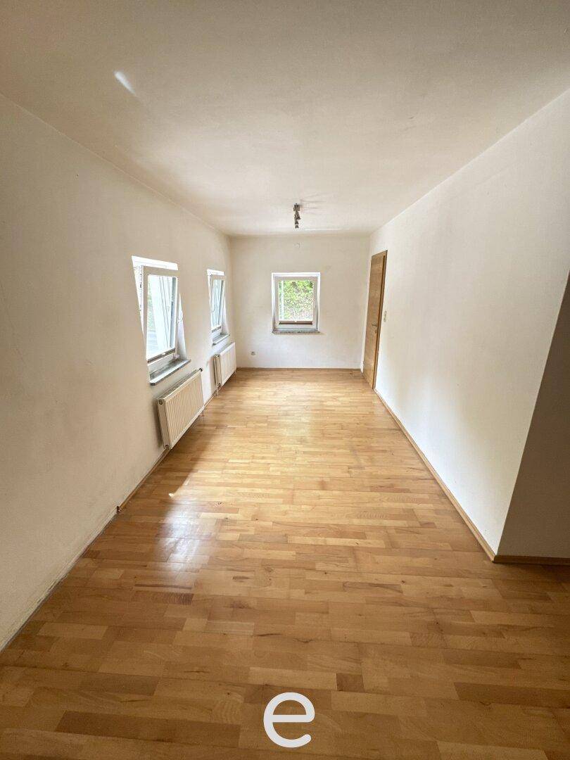 Langes Schlafzimmer mit Holzboden, weißen Wänden und mehreren Fenstern.