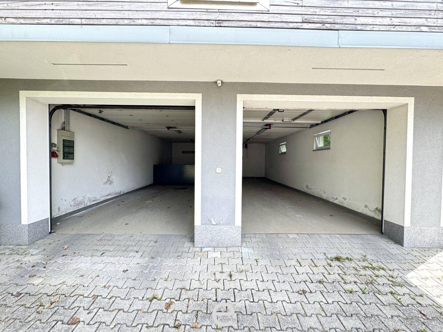 Leere Doppelgarage mit Betonboden und Fenstern, bereit zur Nutzung.