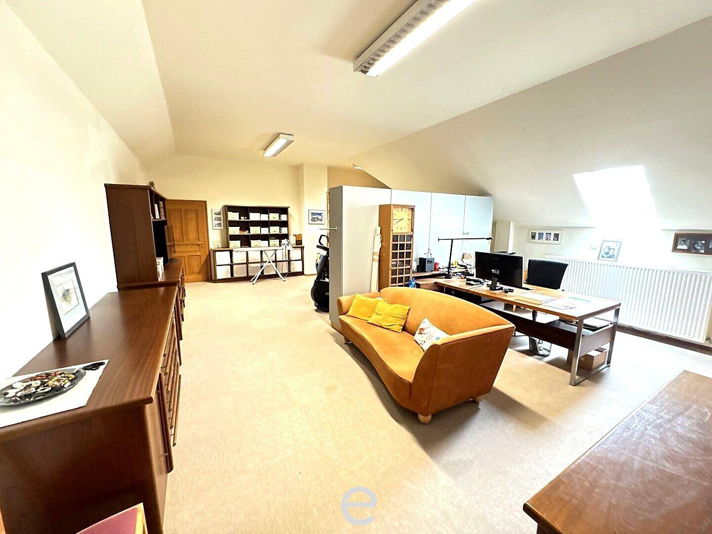 Geräumiges Dachgeschosszimmer, als Büro und Wohnbereich genutzt, mit Dachschrägen und Teppichboden.