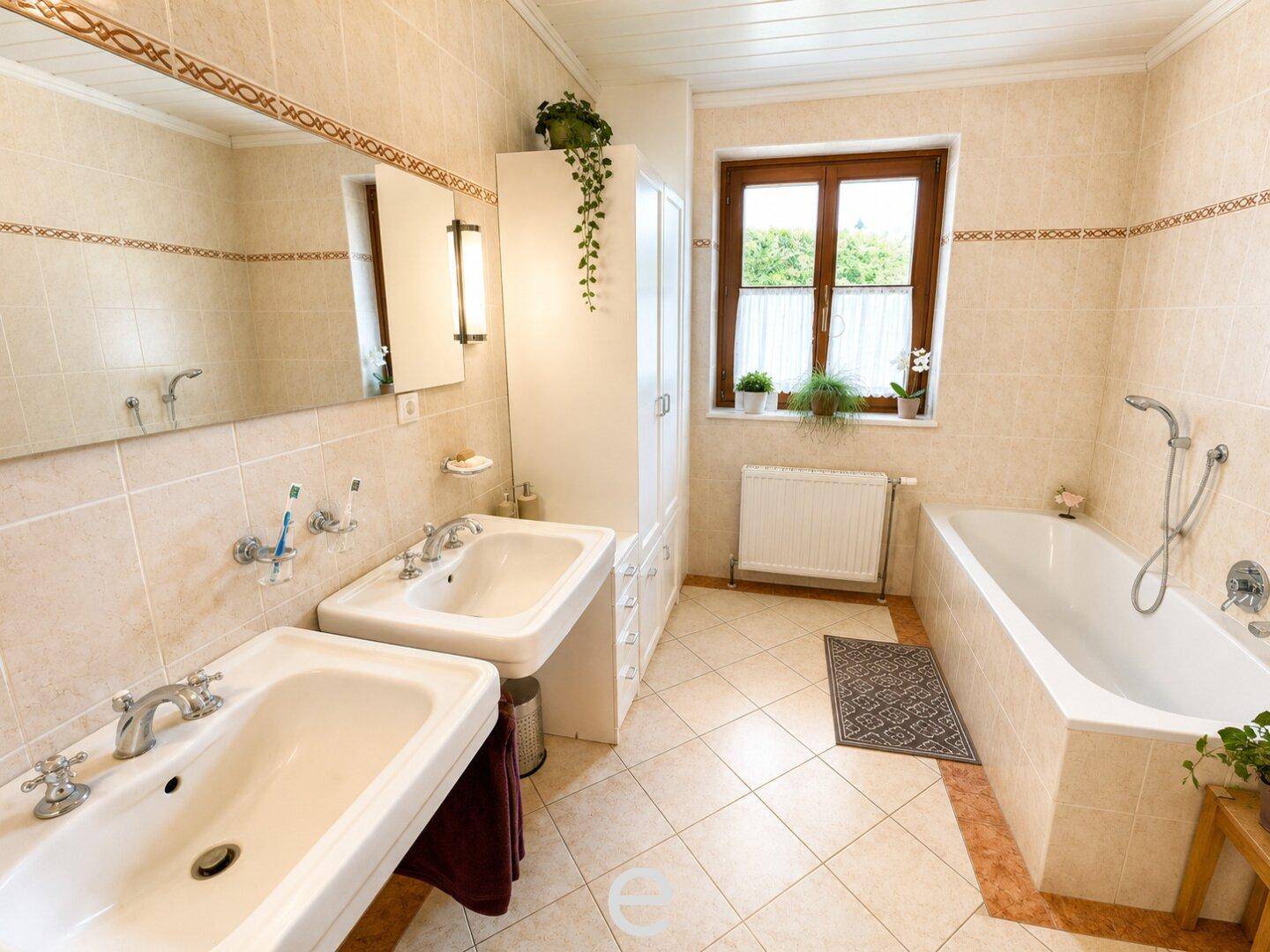 Helles Badezimmer mit Doppelwaschbecken, Badewanne und beigefarbenen Fliesen.