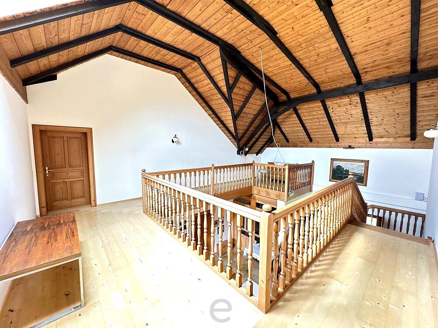 Offener Dachgeschossbereich mit sichtbaren Holzbalken und Treppengeländer aus Holz.
