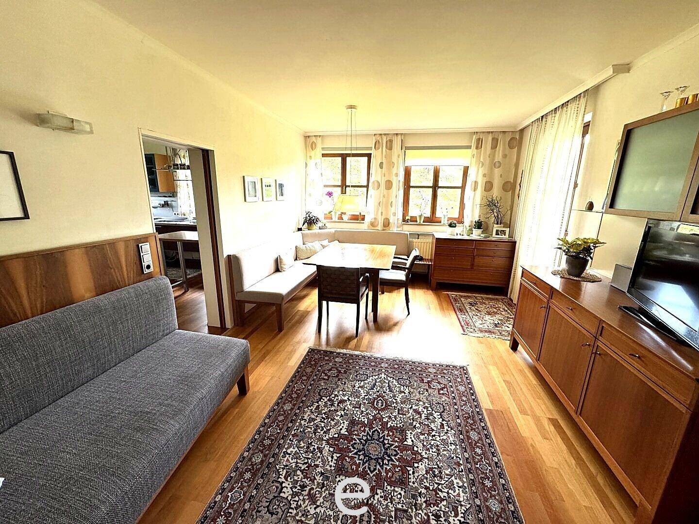 Gemütlicher Wohnbereich mit Sofa, Esstisch und Blick auf den Garten durch die Fenster.