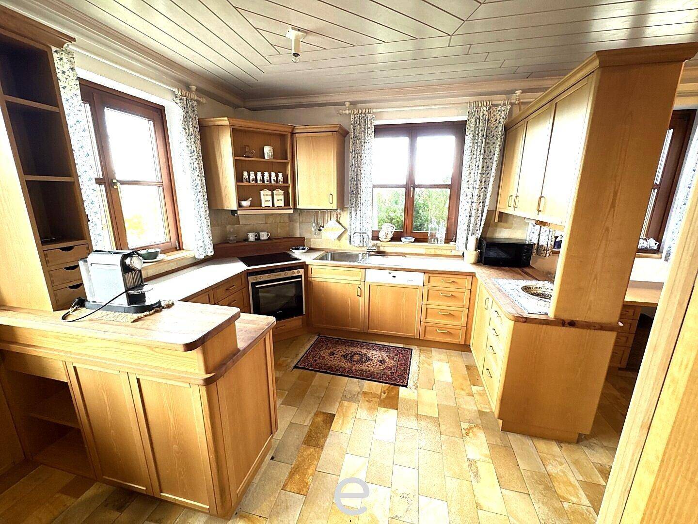 Traditionelle Holzküche mit gefliestem Boden, mehreren Fenstern und viel Stauraum.