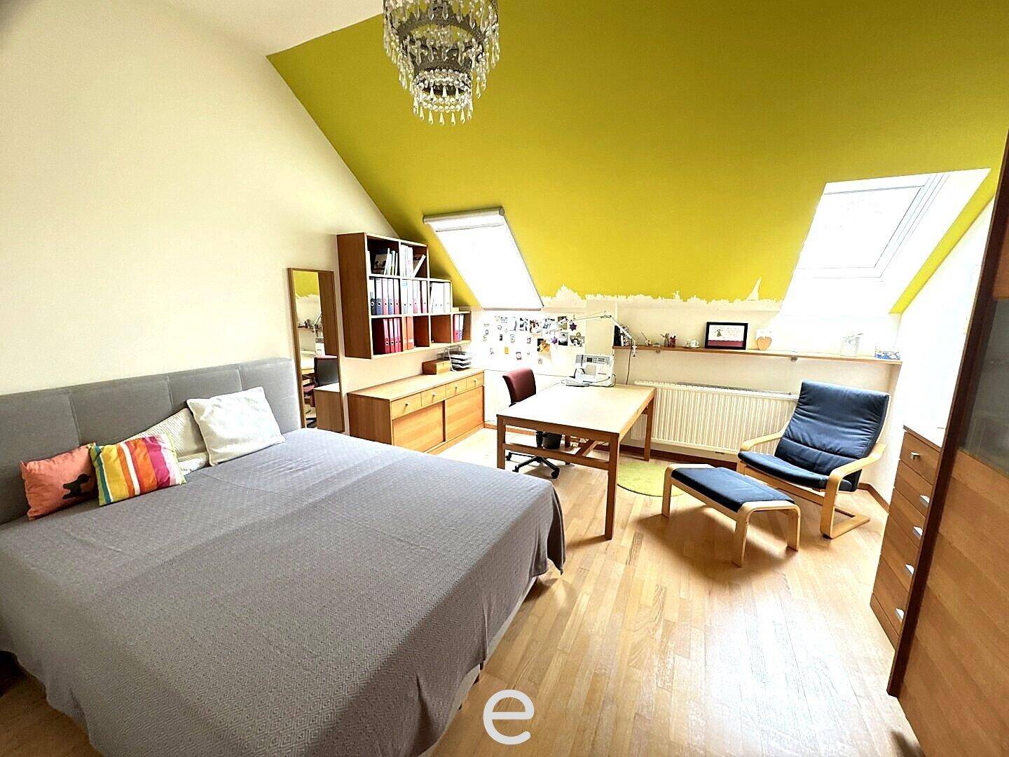 Schlafzimmer im Dachgeschoss mit Bett, Schreibtisch, Dachschrägen und farbiger Wandgestaltung.