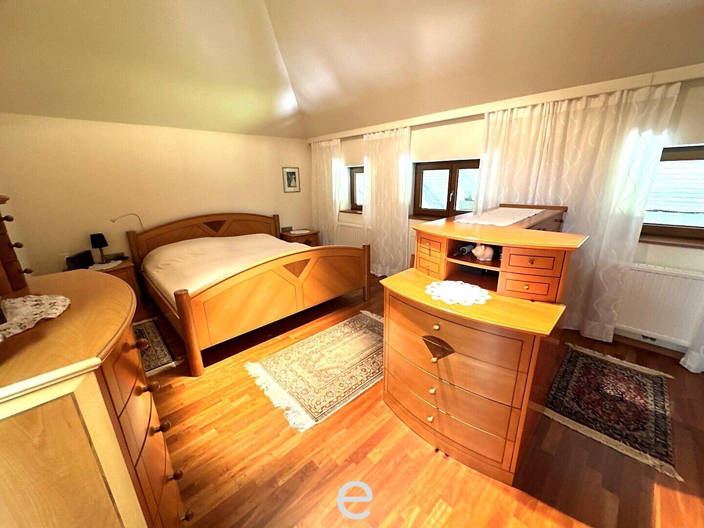 Traditionelles Schlafzimmer mit Holzmöbeln, Holzboden und Fenstern mit Vorhängen.