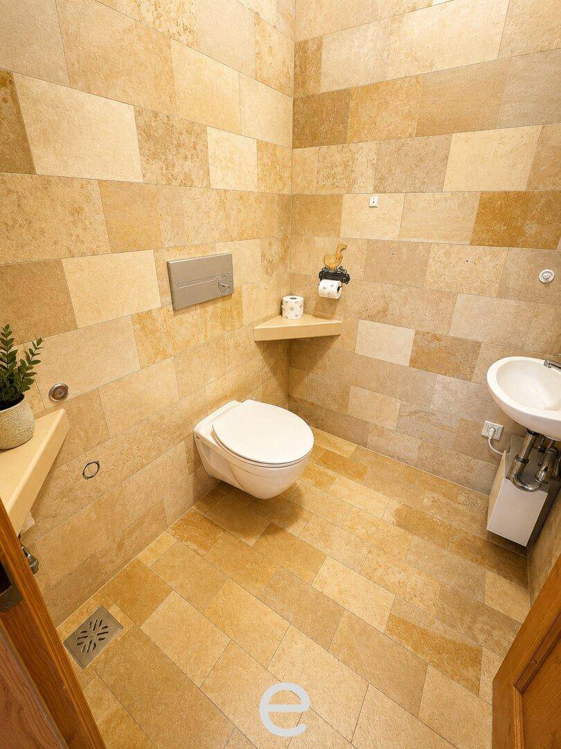 Modern gefliestes Gäste-WC mit wandhängendem WC und kleinem Waschbecken.