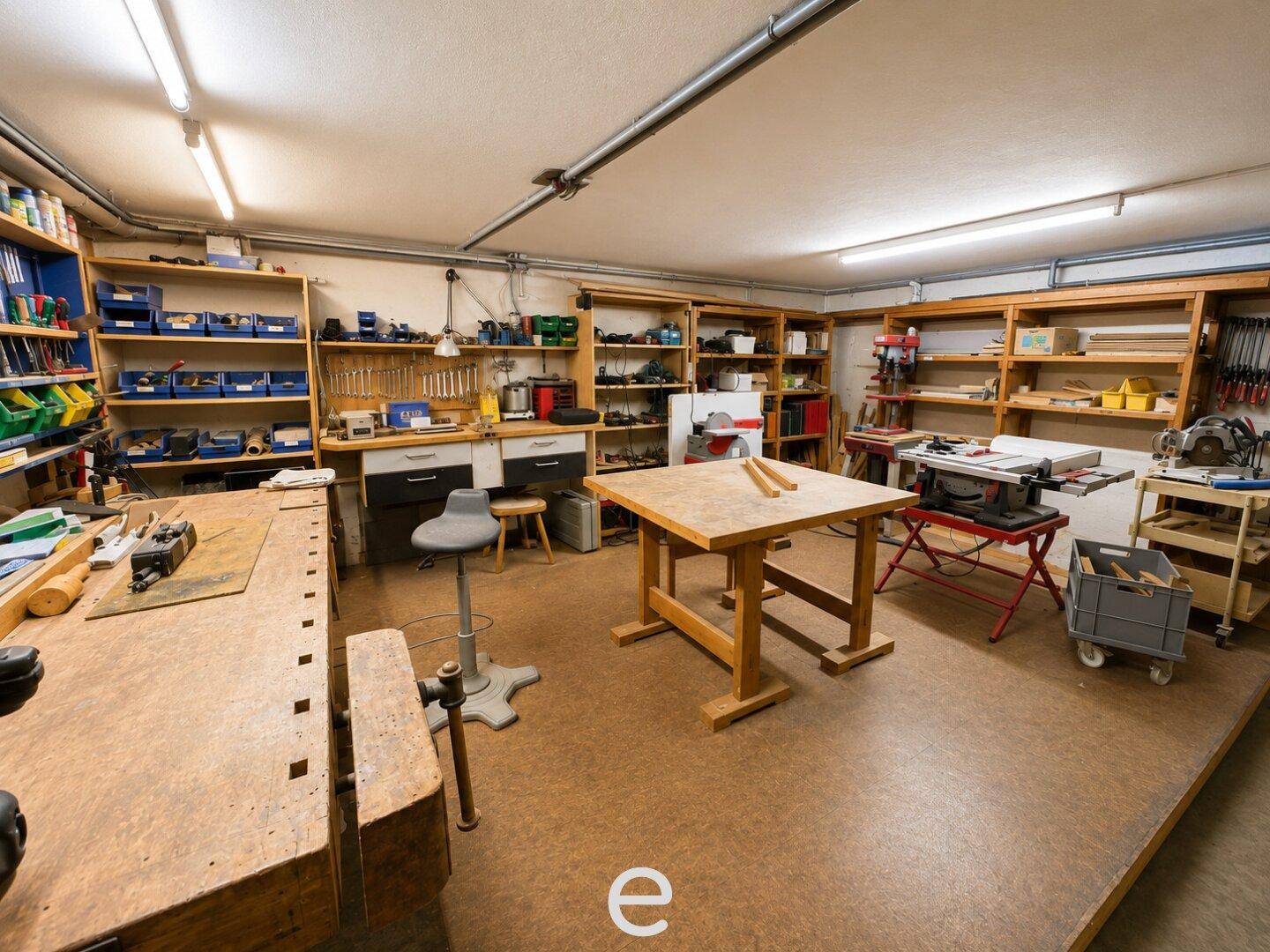 Gut ausgestattete Werkstatt mit mehreren Arbeitsflächen, Regalen und Werkzeugen.