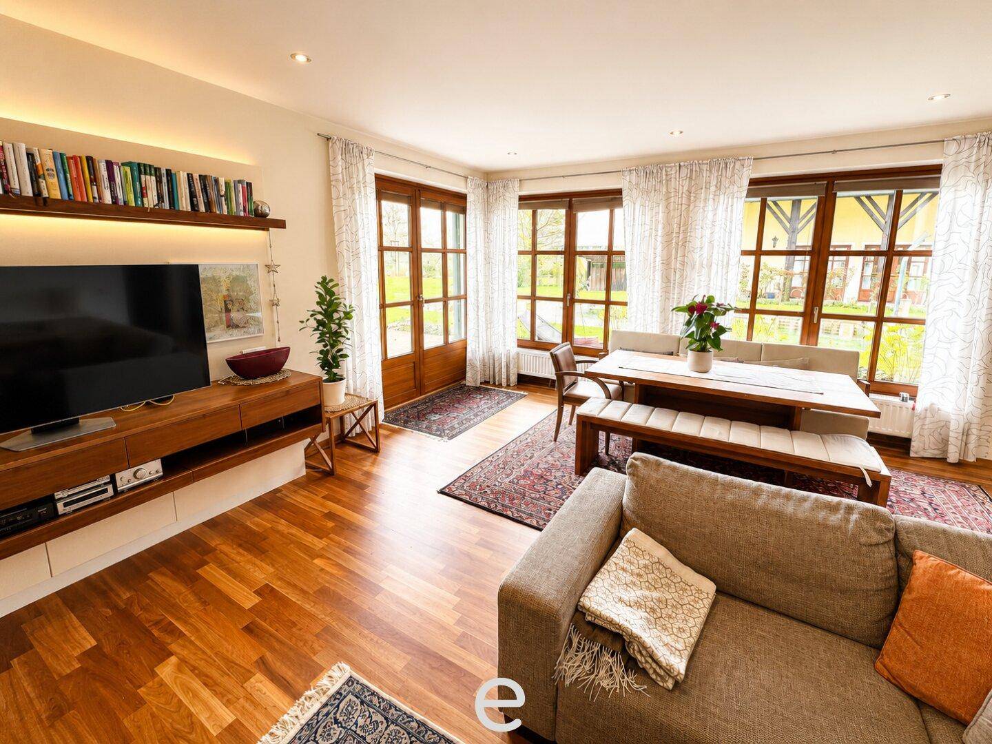 Helles Wohn- und Esszimmer mit Holzboden, großen Fenstern und gemütlicher Einrichtung.