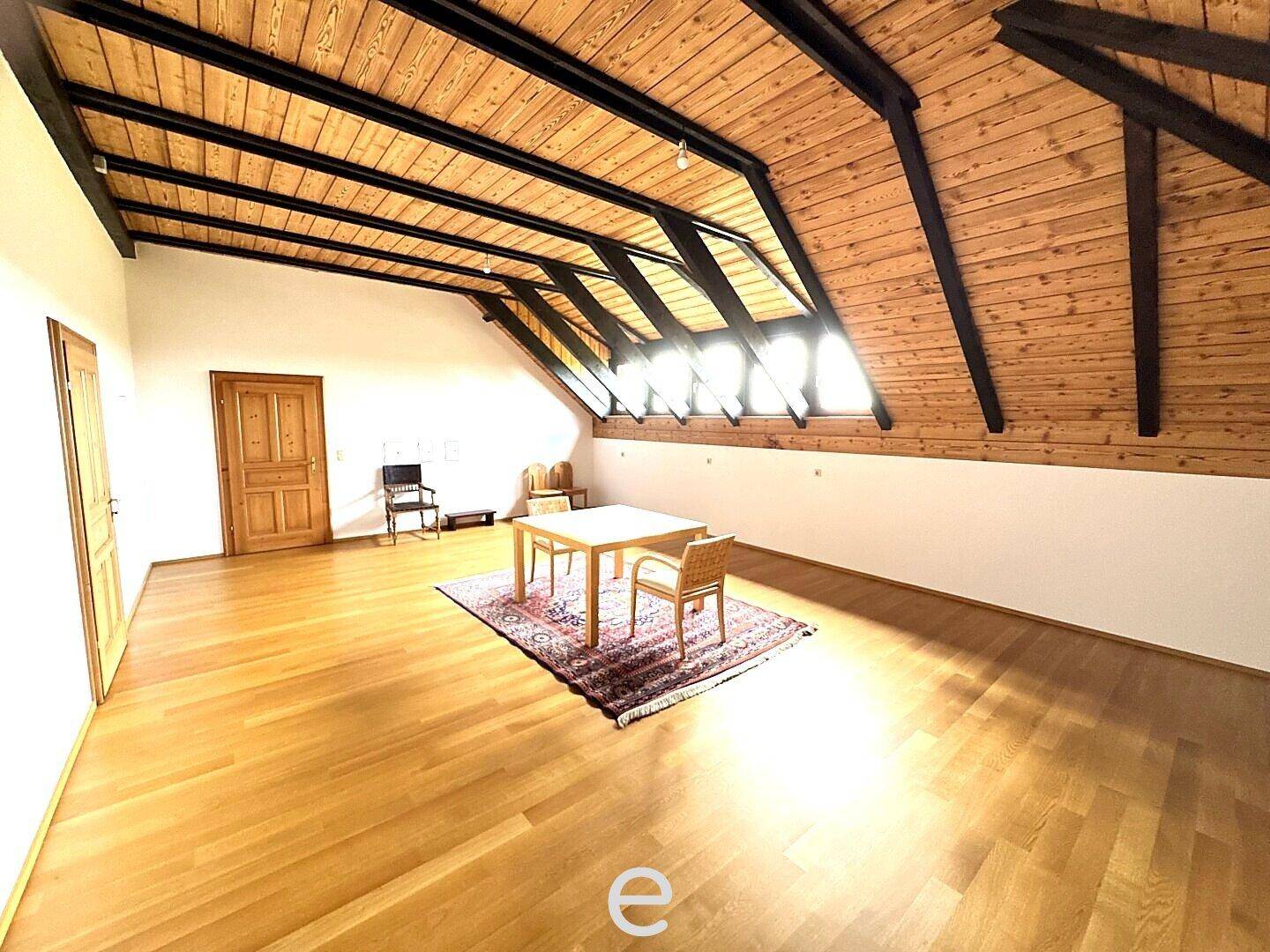 Helles Dachgeschosszimmer mit Holzbalkendecke, Holzboden und großen Dachfenstern.