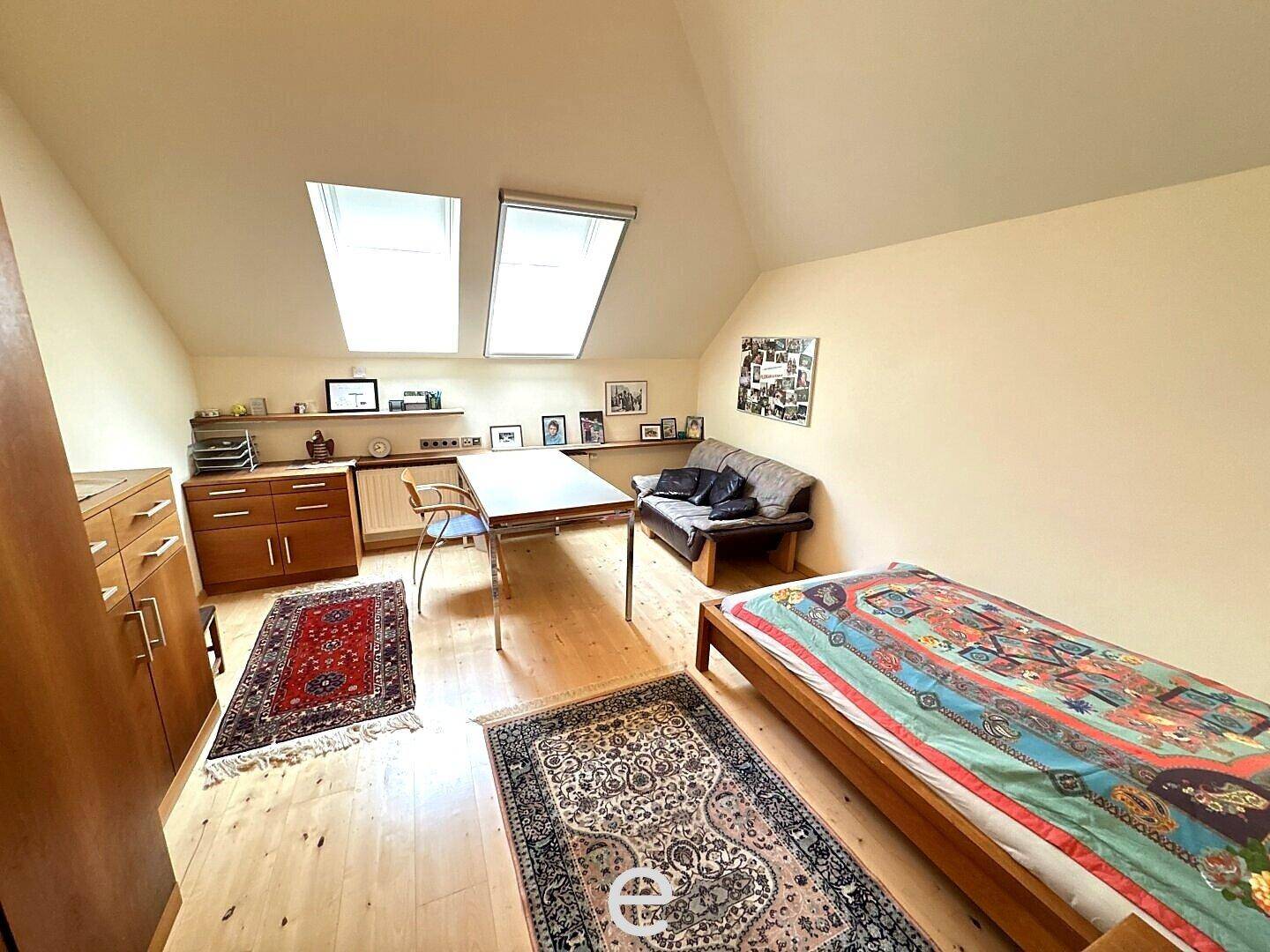 Gemütliches Schlafzimmer im Dachgeschoss mit Bett, Tisch und zwei Dachfenstern.