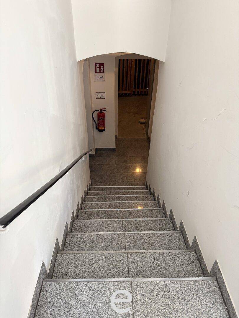 Granittreppe mit Handlauf führt in die unteren Etagen, ein Feuerlöscher ist sichtbar.
