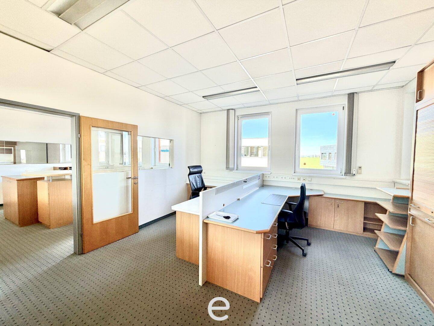 Offener Bürobereich mit mehreren Arbeitsplätzen, Teppichboden und Fenstern für Tageslicht.
