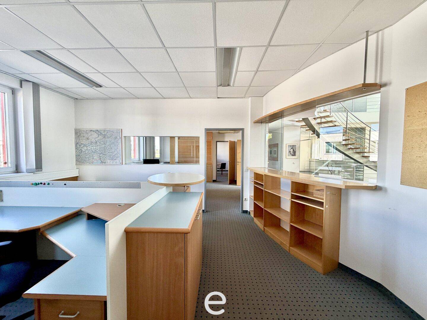 Offener Bürobereich mit Empfangstheke, Schreibtischen und Blick auf eine moderne Treppe.
