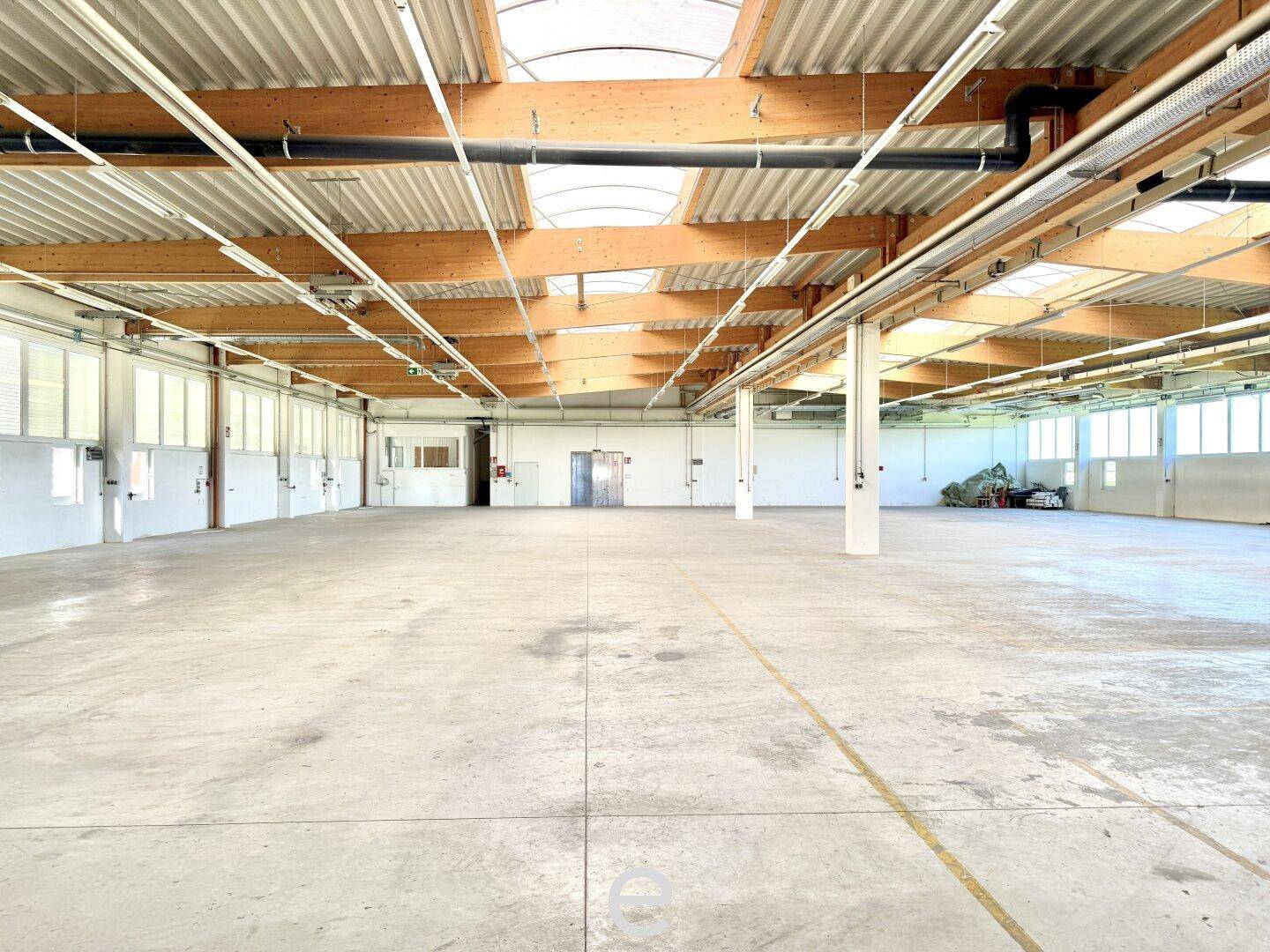 Große, leere Lagerhalle mit hohen Decken, sichtbaren Holzbalken und Oberlichtern für natürliches Licht.
