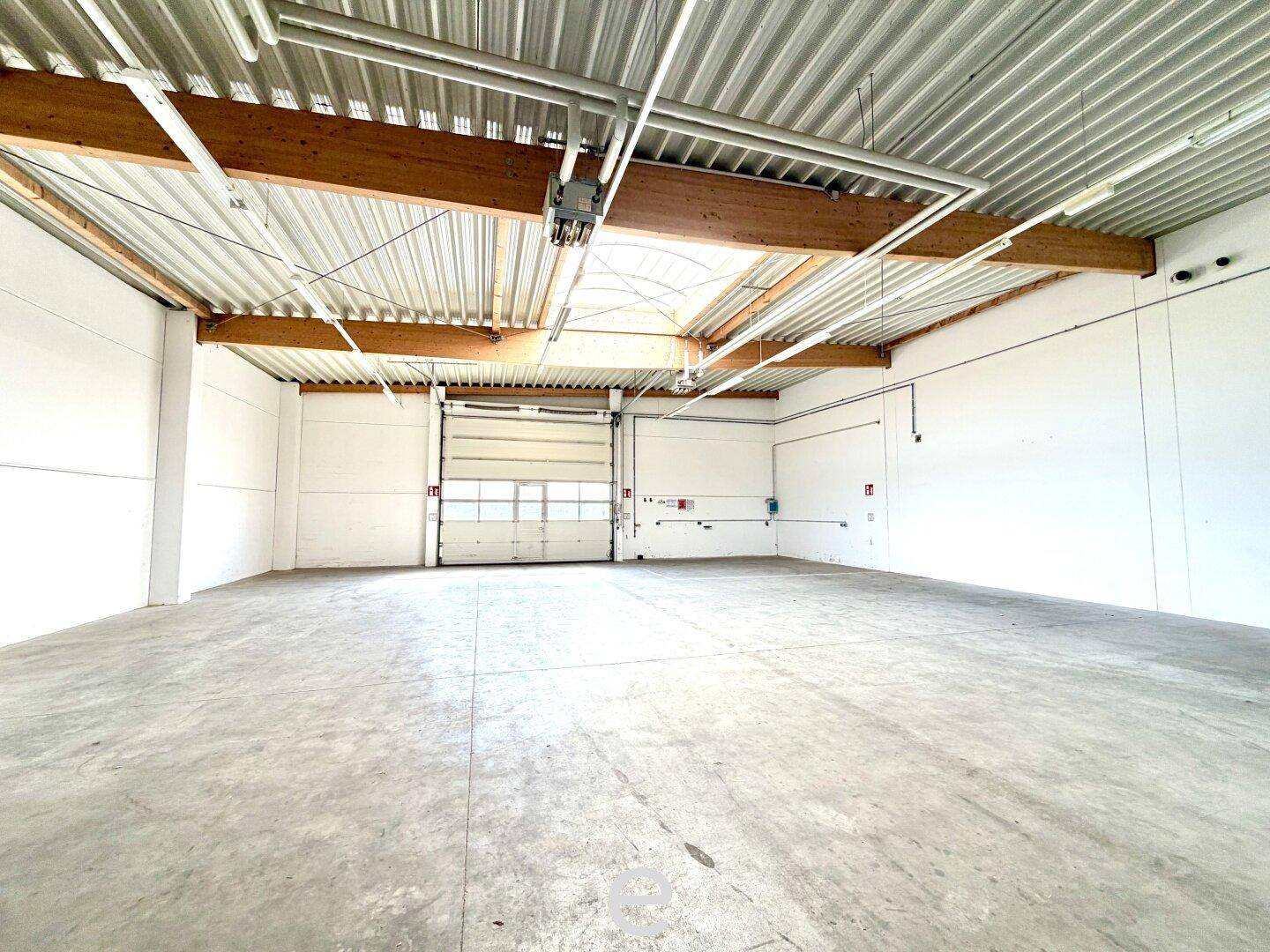 Leere Lagerhalle mit Rolltor, hohen Decken und Oberlichtern, bereit für den Warenumschlag.