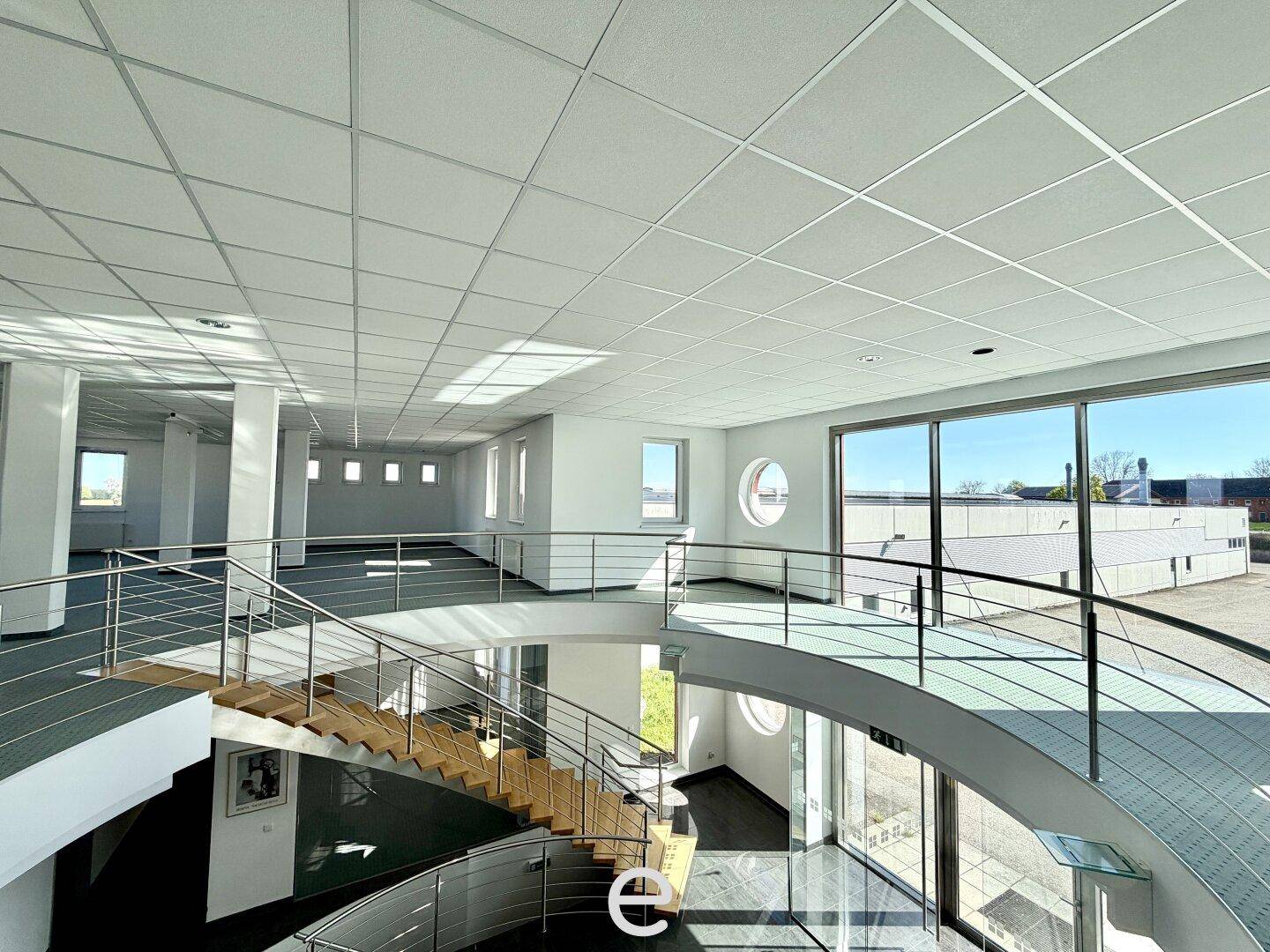 Heller Bürobereich mit einer offenen Galerie, moderner Treppe und großen Fenstern mit Weitblick.