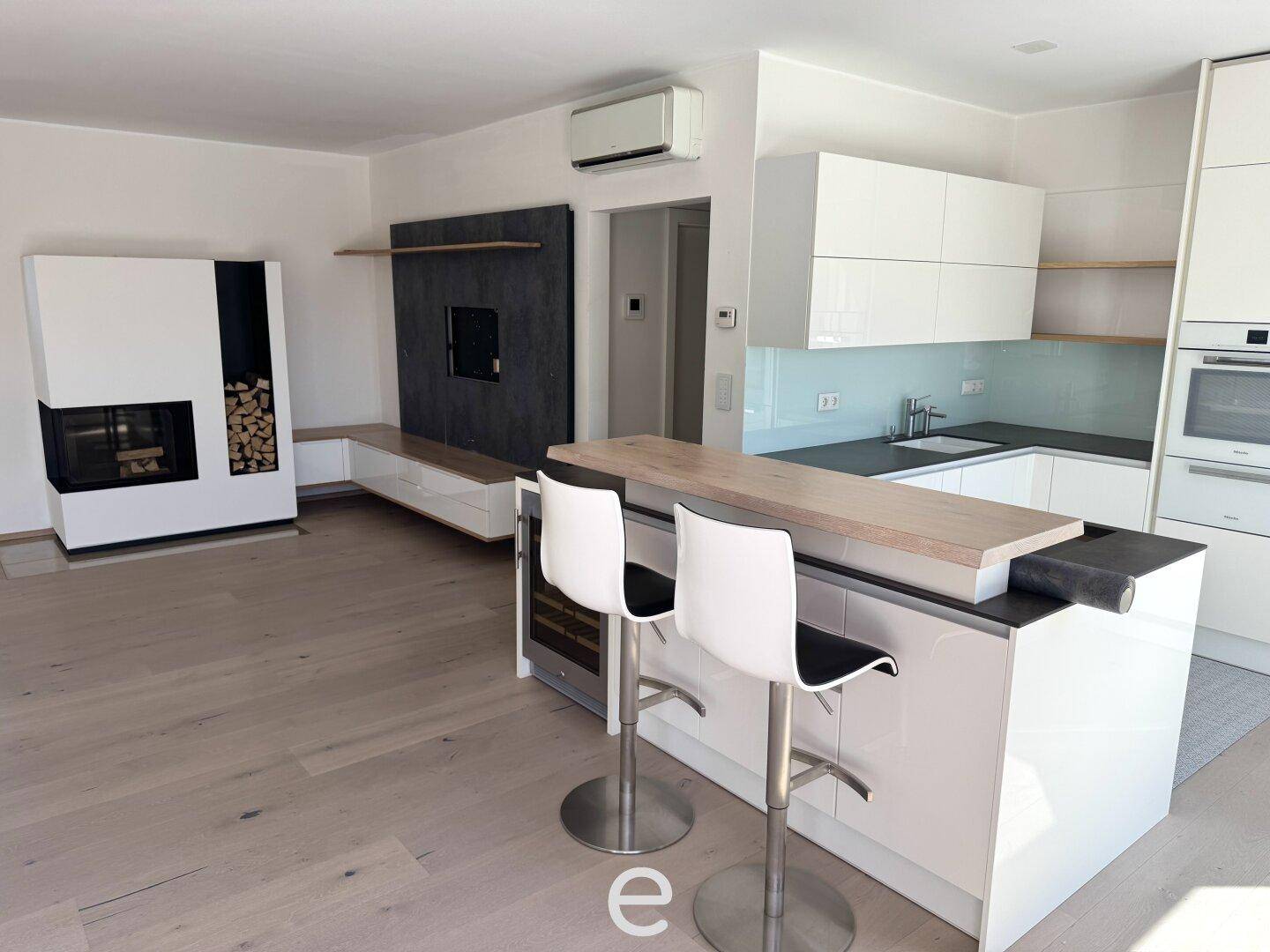 Moderne offene Küche mit Kochinsel, Kamin und hellem Holzfußboden im Wohnbereich.