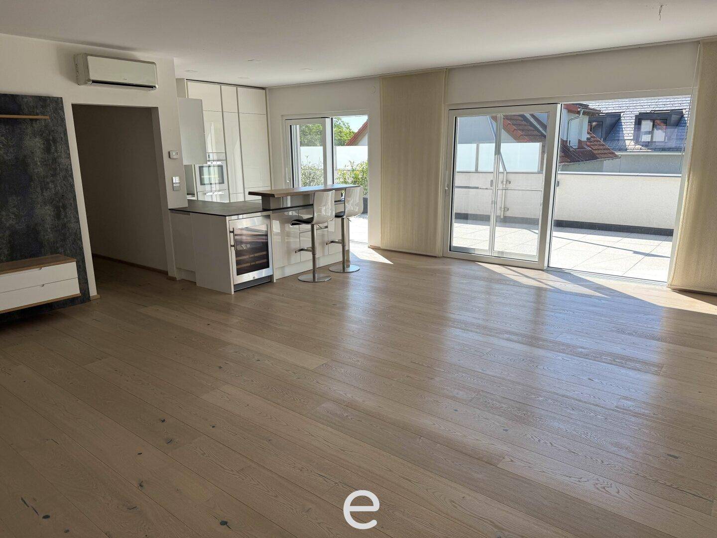 Heller offener Wohnbereich mit Holzboden, Terrassenzugang und integrierter Küchenzeile.