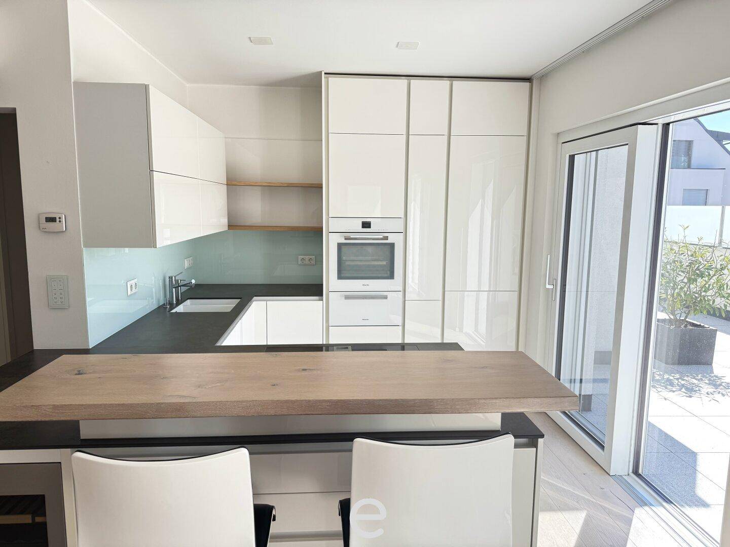 Elegante weiße Küche mit integrierten Geräten, dunklen Arbeitsplatten und Terrassenzugang.