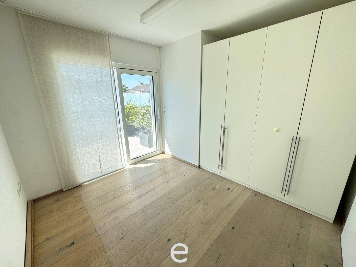Schlafzimmer mit hellem Holzboden, großem Einbauschrank und Zugang zur Terrasse.