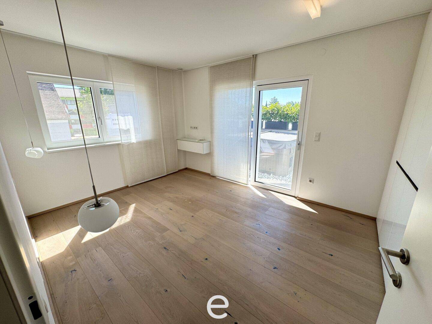 Helles Schlafzimmer mit Holzboden, Fenster und Zugang zu einem Außenbereich.