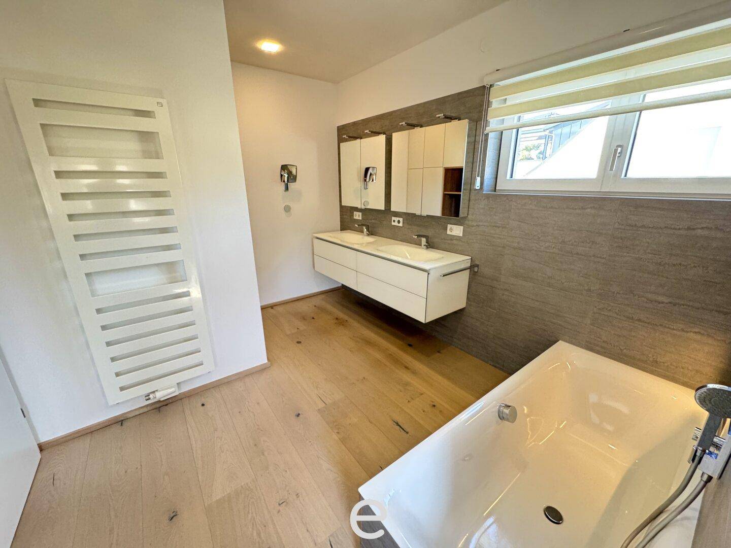Helles Badezimmer mit Doppelwaschbecken, beheiztem Handtuchhalter und Badewanne.