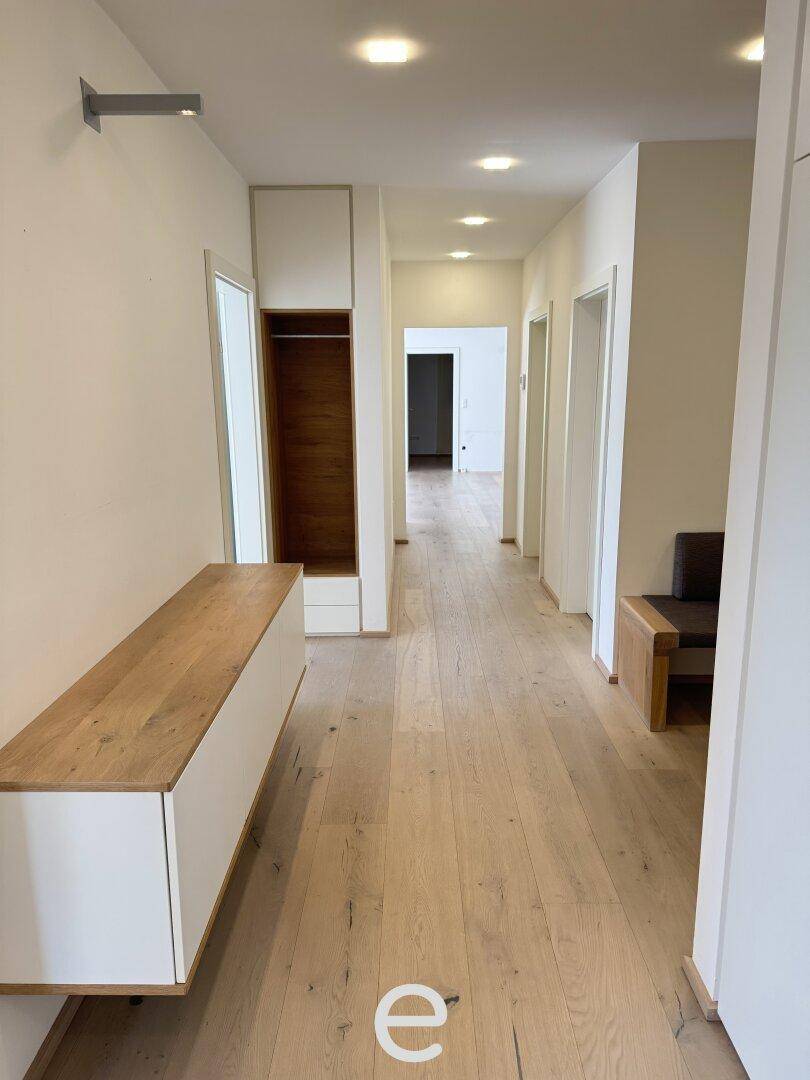 Langer Flur mit hellem Holzfußboden, integrierten Schränken und moderner Beleuchtung.