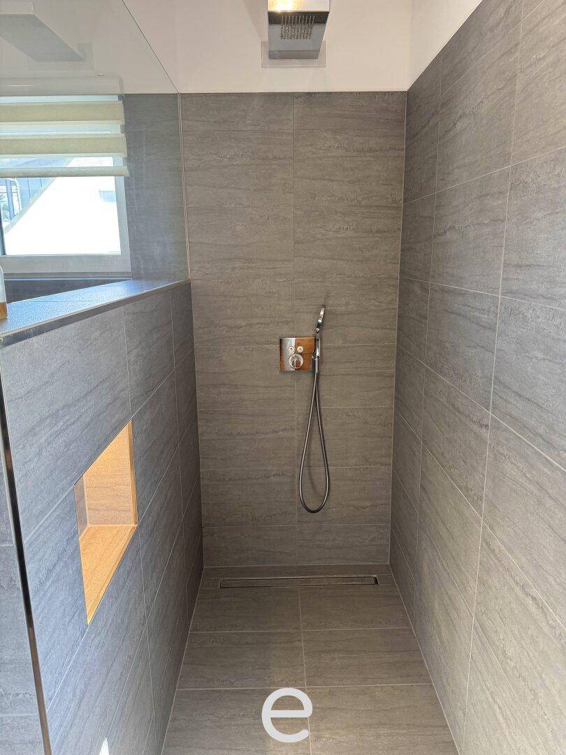 Moderne begehbare Dusche mit grauen Fliesen und Regenduschkopf für entspannende Momente.