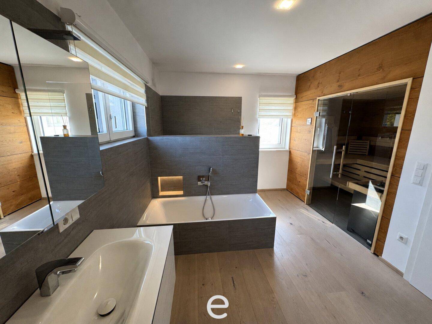 Geräumiges Badezimmer mit Badewanne, Doppelwaschbecken, Holzverkleidung und integrierter Sauna.