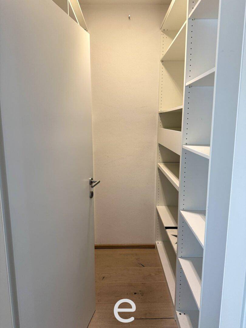 Praktischer begehbarer Kleiderschrank mit weißen Regalsystemen für viel Stauraum.