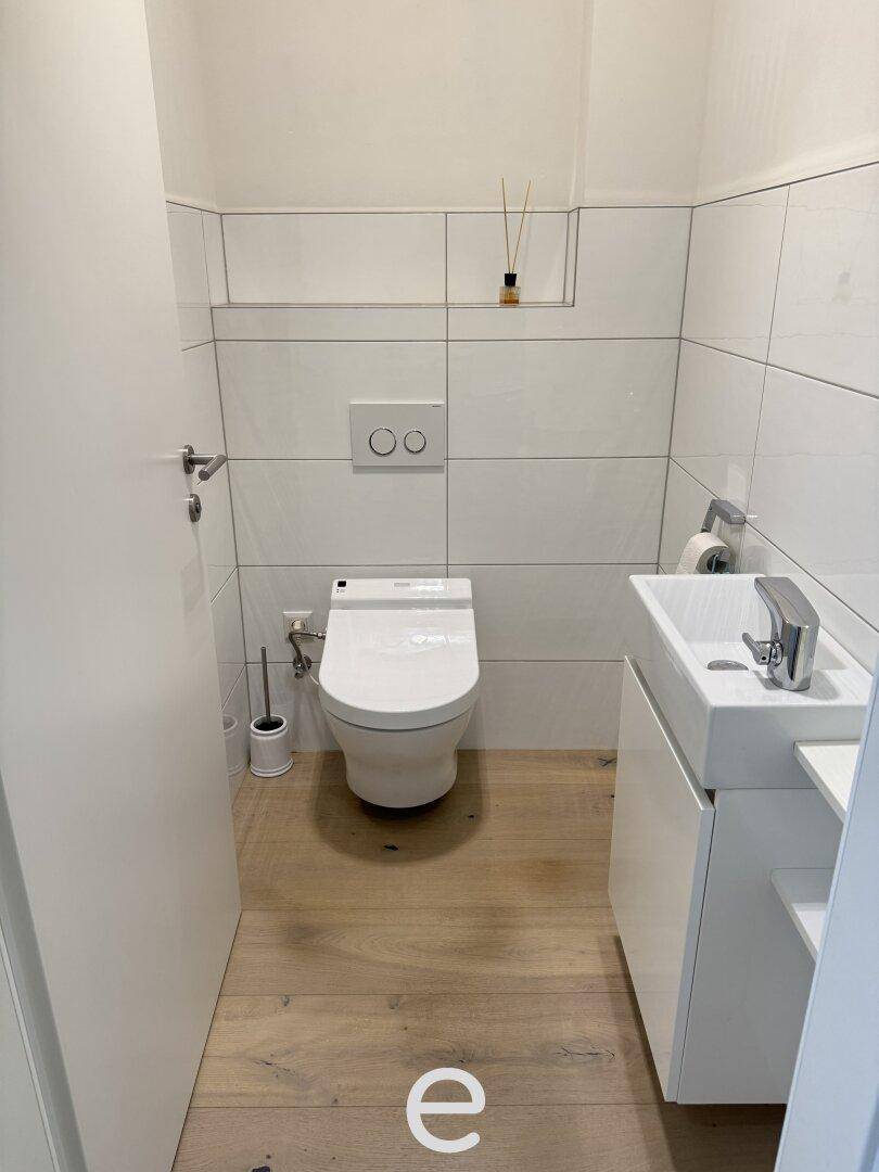 Modernes Gäste-WC mit wandhängender Toilette, kleinem Waschbecken und weißen Fliesen.