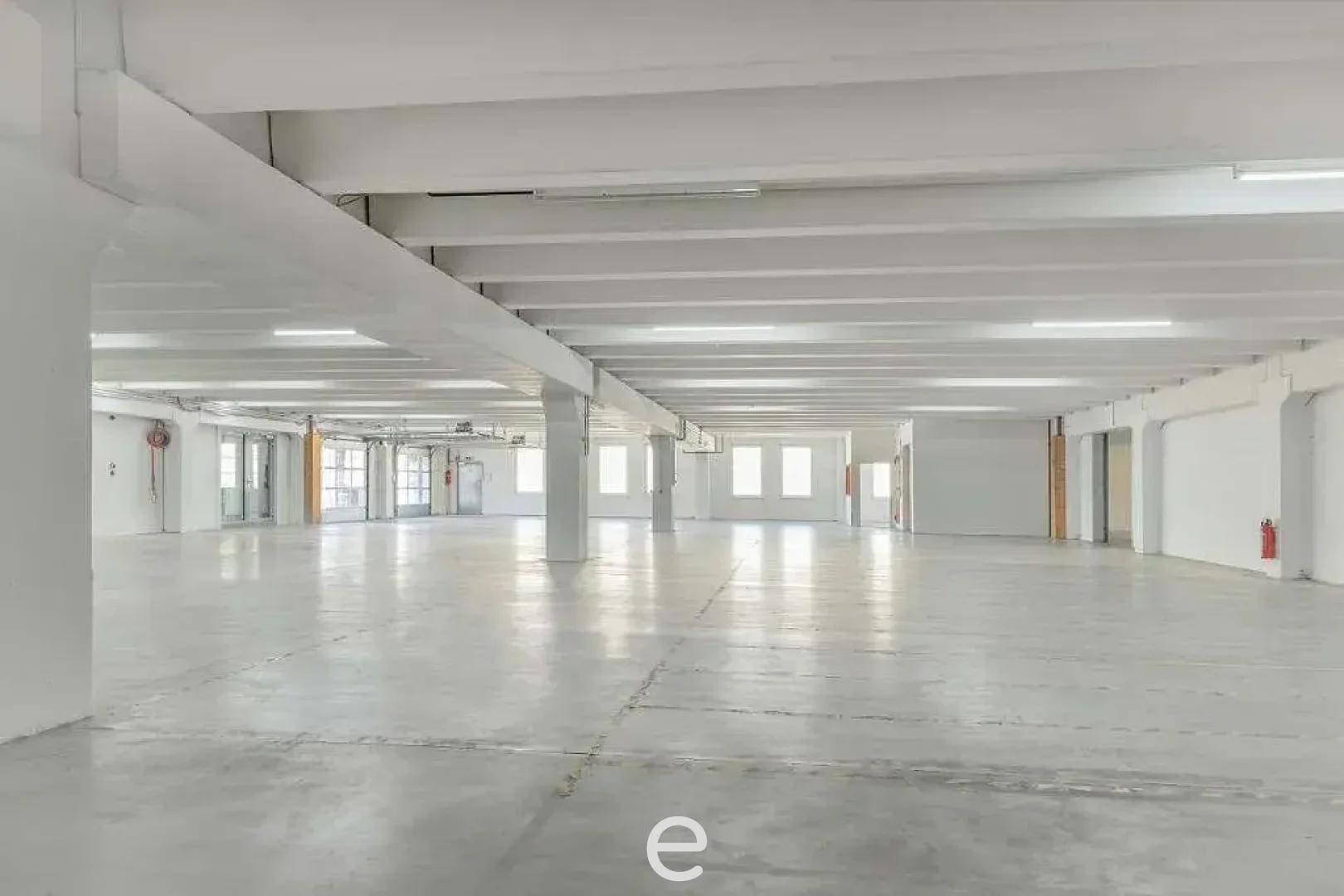Weitläufiger, leerer Gewerberaum mit hohen Decken und vielen Fenstern, bietet vielseitige Nutzungsmöglichkeiten.