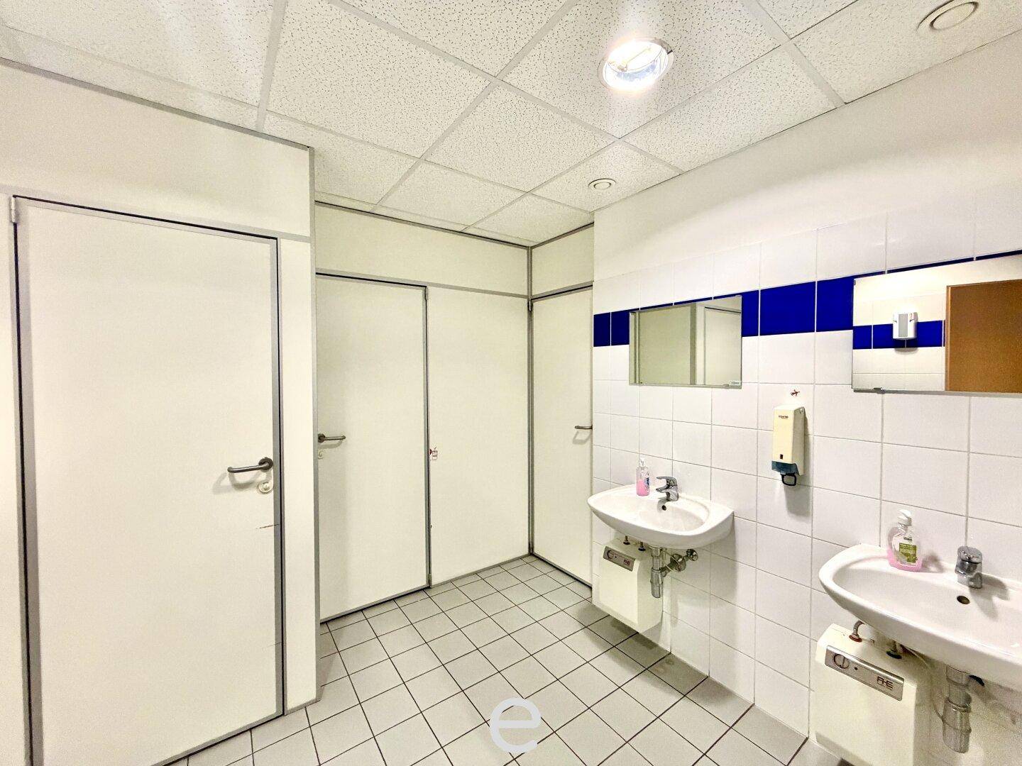 Öffentliche Toilettenanlage mit mehreren Waschbecken und weiß-blauen Fliesen.