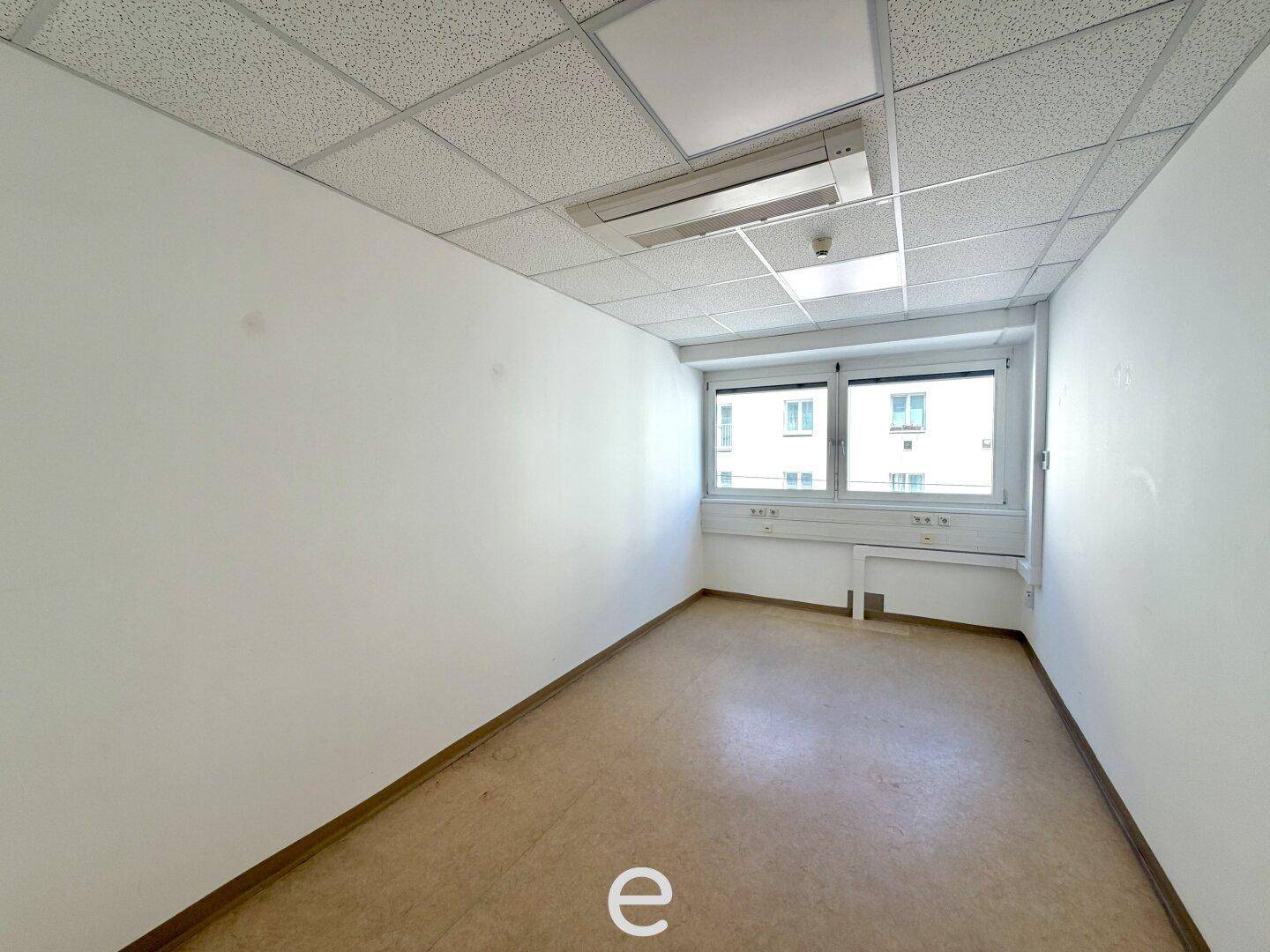 Kleineres, leeres Büro mit einem Fenster, abgehängter Decke und hellem Linoleumboden.