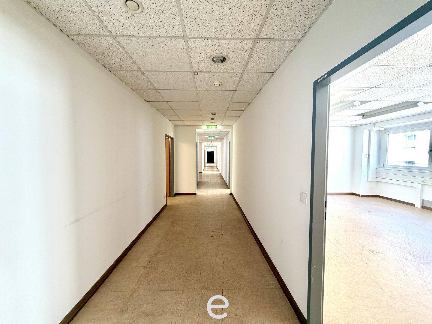 Heller Büroflur mit Linoleumboden, der zu weiteren Büroräumen führt.
