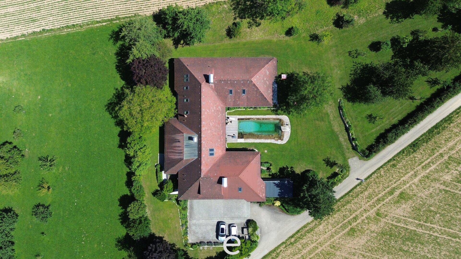 Draufsicht des Anwesens mit L-förmigem Gebäude, Pool und weitläufigem Grundstück.