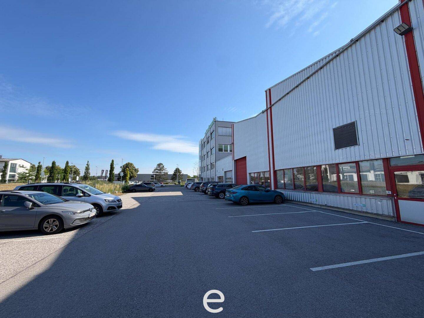 Außenansicht des Industriegebäudes mit großem Parkplatz und blauer Himmel.